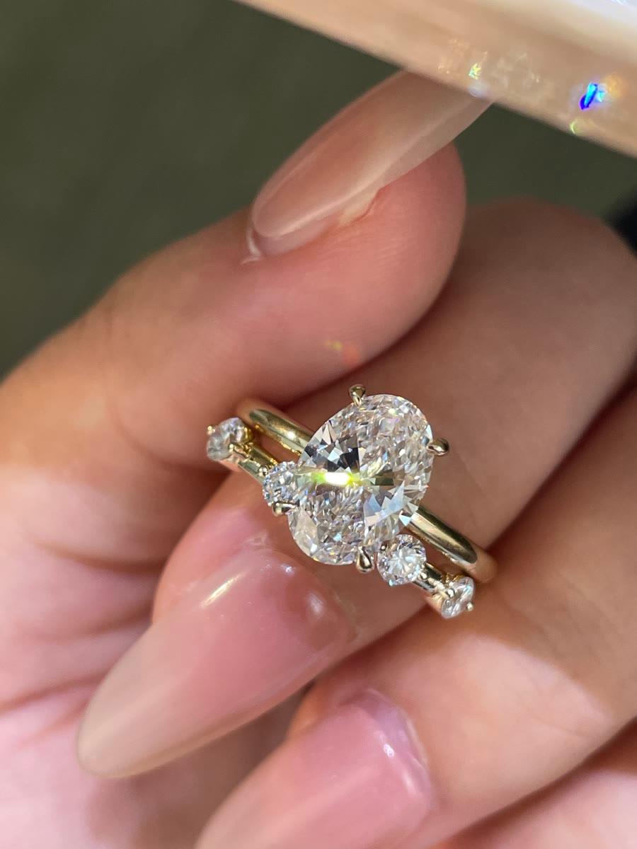 A finished oval diamond ring with shoulder stones, held in hand