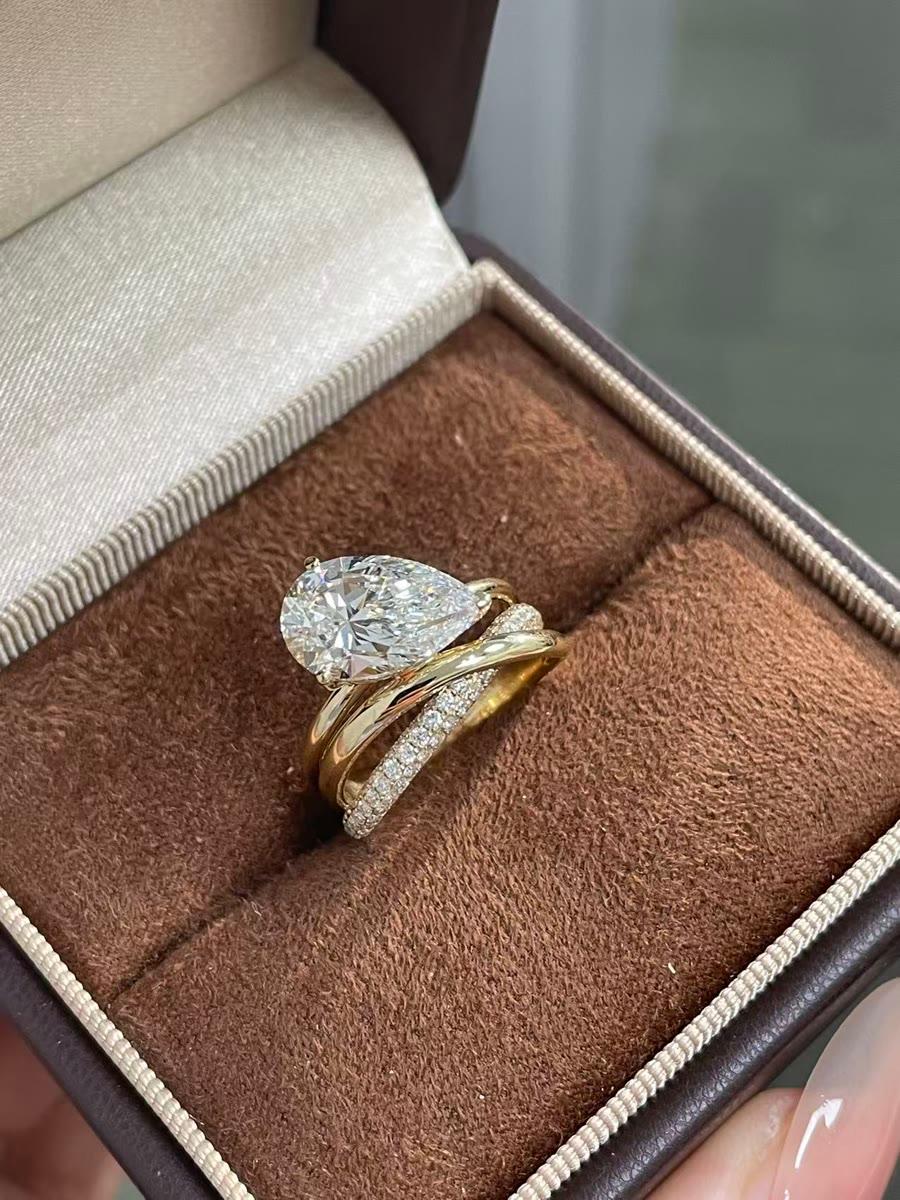 A finished pear-cut solitaire ring with a twisted pavé band, presented in a jewelry box